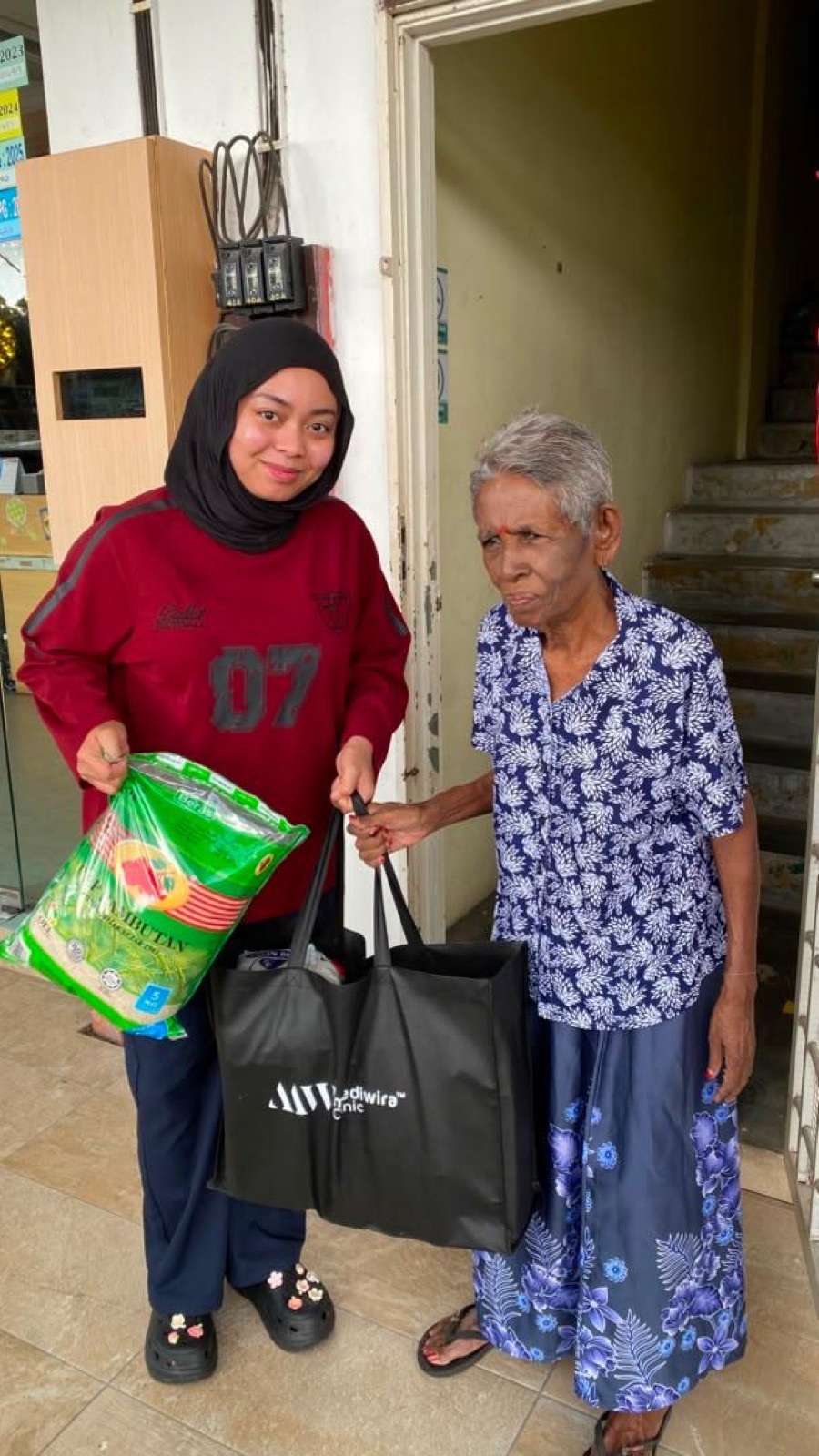 A Mediwira volunteer delivering rice and groceries to an elderly resident at her doorstep