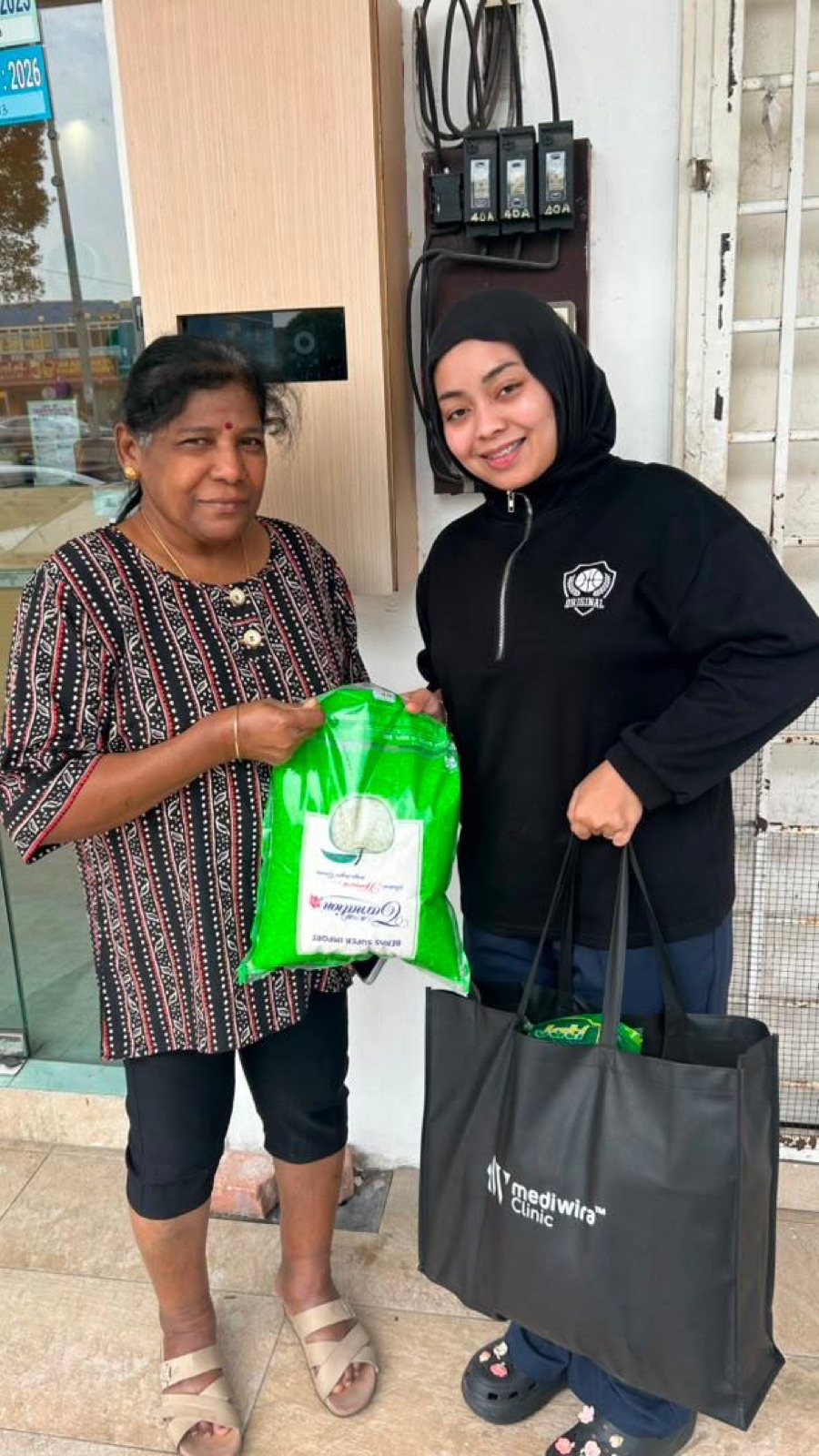 A Mediwira volunteer handing rice and a grocery bag to an elderly resident outside a clinic