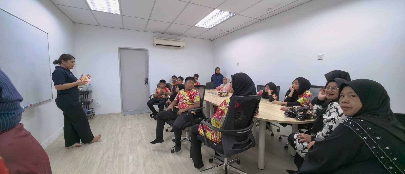Wide view of the classroom with children in red batik shirts and their guardians listening to the dental talk