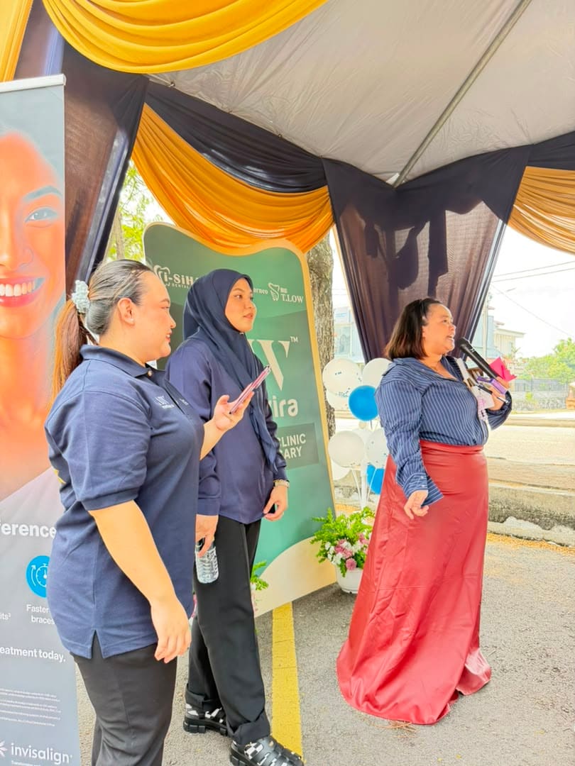 Staff and a speaker with a handheld microphone beside the Invisalign banner and the anniversary backdrop