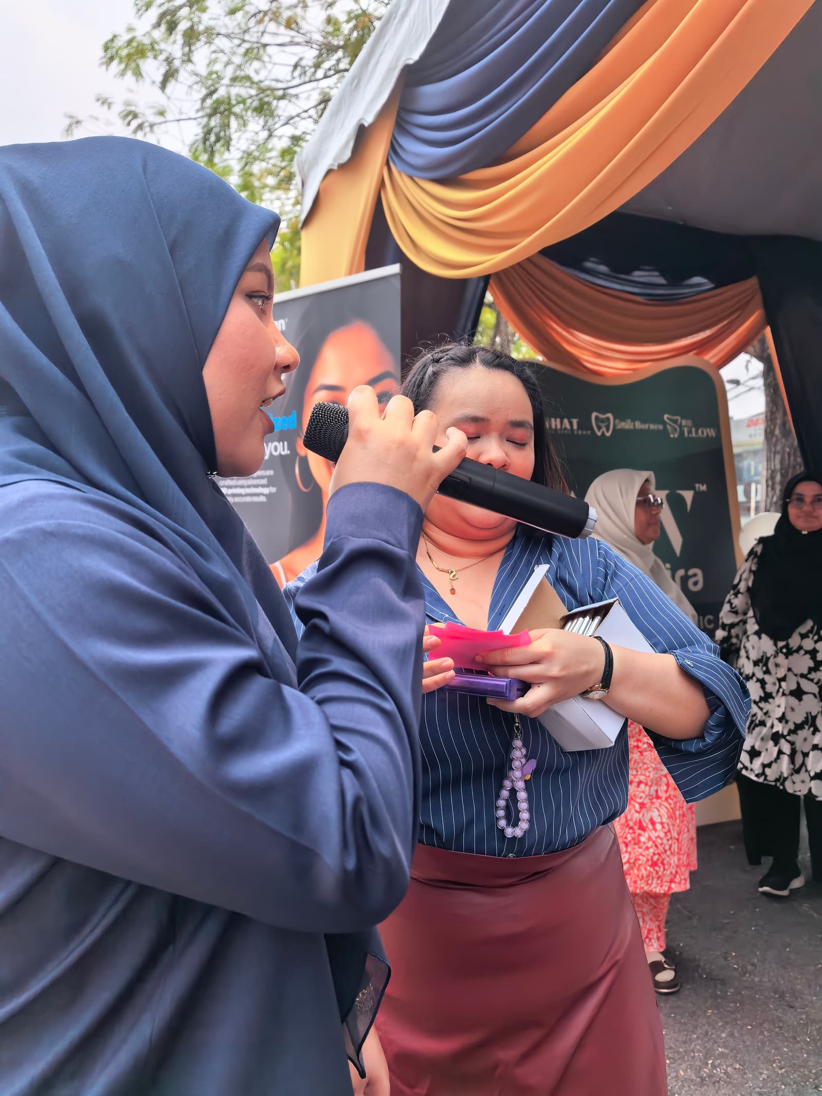 A speaker addressing guests near the i-SiHAT, Smile Borneo and T.LOW backdrop